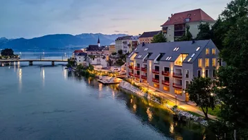 Moderne Gebäude am Flussufer bei Sonnenuntergang mit Bergblick und Stadtkulisse.
