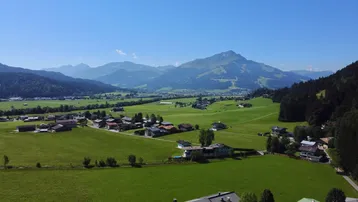 Weitläufige Landschaftsaufnahme eines Tals mit Dorf, grünen Feldern und majestätischen Bergen.