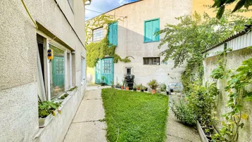 Kleiner Hinterhofgarten zwischen Gebäuden mit grüner Rasenfläche und Pflanzenbewuchs an der Fassade.