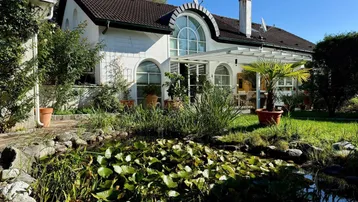 Charmantes Haus mit großem Garten, Teich und üppiger Vegetation unter blauem Himmel.