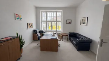 Privates Büro mit großem Fenster, Schreibtisch und einer klassischen schwarzen Ledercouch.