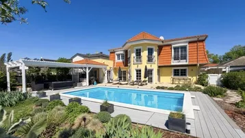 Großzügiger Gartenbereich mit Swimmingpool, Sonnenterrasse und Pergola vor dem gelben Haus.