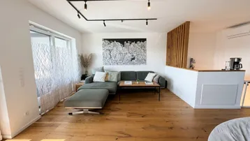 Helles Wohnzimmer mit Holzboden, modernem Sofa und offener Gestaltung zum Essbereich.