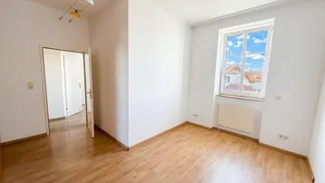 Helles Zimmer mit Holzboden, weißen Wänden und Blick auf die Dächer, ideal als Wohn- oder Schlafzimmer.