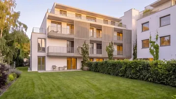 Modernes Mehrfamilienhaus mit Balkonen, gepflegtem Rasen und Hecken im Vordergrund.