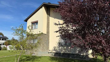 Einfamilienhaus mit heller Fassade, Steindetails und gepflegtem Vorgarten unter blauem Himmel.