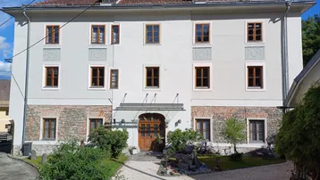 Historisches Gebäude mit traditioneller Architektur, Steinsockel und vielen Holzfenstern.