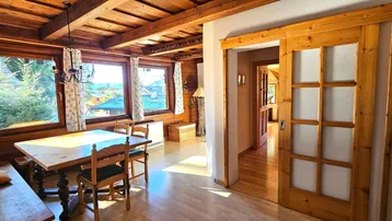 Gemütlicher Essbereich mit Holztisch, Holzvertäfelung und großen Fenstern, die viel Licht hereinlassen.
