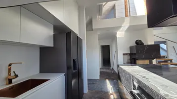 Detailansicht der modernen Küche mit goldenem Wasserhahn, integriertem Kühlschrank und dunklem Fischgrätparkett.