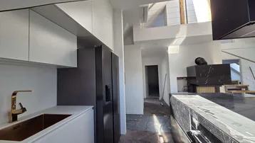 Helle Küche mit weißen Schränken, schwarzem Kühlschrank und goldener Armatur neben der Marmorinsel.
