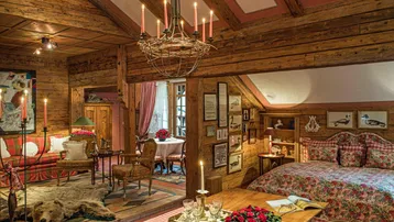 Gemütliches Wohnzimmer im alpinen Stil mit Holzbalken, Kamin und traditionellen Möbeln.