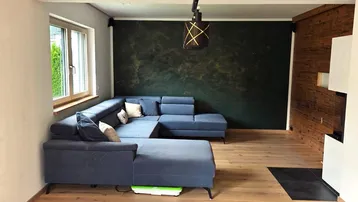 Gemütliches Wohnzimmer mit großem Ecksofa, Holzwand und dunkler Akzentwand.