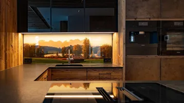 Moderne Küche mit Holzelementen, integrierten Geräten und einer beleuchteten Rückwand mit Landschaftsmotiv.