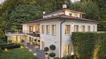 Elegantes Einfamilienhaus mit weitläufigem Garten, mehreren Terrassen und umgeben von üppigem Grün.