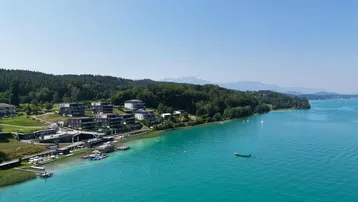 Weitläufiger Blick über den See und die bewaldete Landschaft mit der modernen Wohnanlage am Ufer.