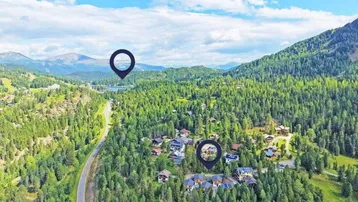 Luftaufnahme einer bewaldeten Berglandschaft mit See, Straße und mehreren Chalets.