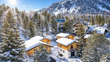 Winterlandschaft mit mehreren schneebedeckten Chalets und verschneiten Bäumen in den Bergen.