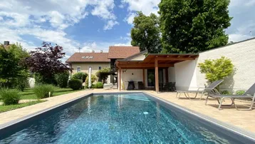 Großer Außenpool mit gepflasterter Terrasse und überdachtem Sitzbereich im gepflegten Garten.