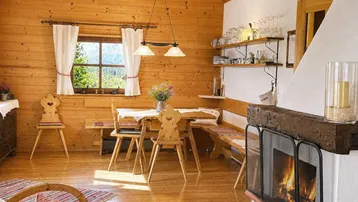 Gemütlicher Wohn- und Essbereich im alpinen Stil mit Holzwänden, Kamin und traditionellen Möbeln.