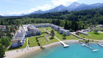 Sommerliche Luftaufnahme einer Wohnanlage am See mit grünen Rasenflächen und Bootsstegen.