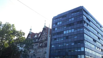 Die Aufnahme zeigt eine moderne Bürogebäude-Fassade neben einem traditionellen Altbau mit Fachwerkelementen.