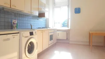 Funktionale Küche mit hellen Schränken, Spülmaschine, Waschmaschine und einem Fenster für Tageslicht.