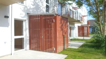 Außenansicht eines modernen Wohngebäudes mit Terrassen, Balkonen und grüner Rasenfläche.