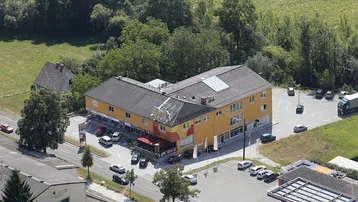 Luftaufnahme eines großen Gewerbegebäudes mit Parkplätzen und umgeben von viel Grün.