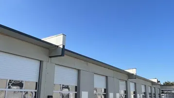 Reihe von Gewerbeeinheiten mit weißen Rolltoren und gepflastertem Vorplatz unter blauem Himmel.
