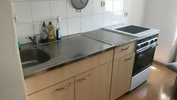 Funktionale Küche mit Holzschränken, Edelstahlspüle und weiß gefliestem Spritzschutz.
