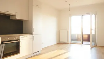 Helle offene Küche mit Holzboden und Zugang zu einem Balkon, ideal für modernes Wohnen.