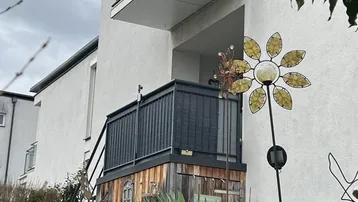 Außenansicht eines Gebäudes mit Balkon und einer Holzkonstruktion im Gartenbereich.