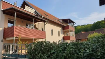 Mehrfamilienhaus mit mehreren Balkonen und Dachschrägen in sonniger Lage.