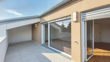 Geräumige Dachterrasse mit Fliesenboden und Zugang zu einem hellen Innenraum.