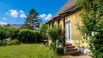 Gelbes Haus mit überdachtem Eingangsbereich und grünem Garten unter blauem Himmel.