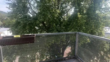Heller Balkon mit Fliesenboden und Metallgeländer, bietet einen schönen Blick ins Grüne.