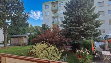 Blick vom Balkon auf den Gemeinschaftsgarten und das gegenüberliegende Wohngebäude mit Bäumen.