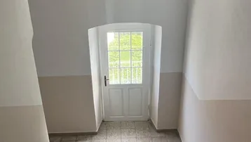 Treppenhaus mit gefliestem Boden und einer hellen Tür, die ins Freie führt.