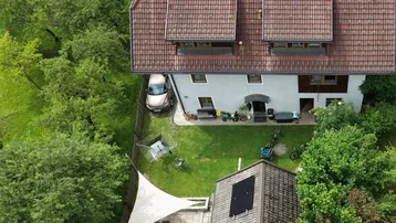 Luftaufnahme eines Hauses mit großem Garten, Terrasse und Sonnensegel, umgeben von viel Grün.