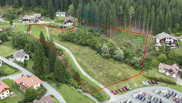 Luftaufnahme eines großen Grundstücks, umgeben von Wald und einigen Häusern, mit einem Feldweg und Parkplätzen.