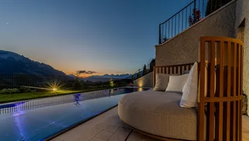 Gemütliche Outdoor-Lounge mit Infinity-Pool und atemberaubendem Bergblick bei Sonnenuntergang.