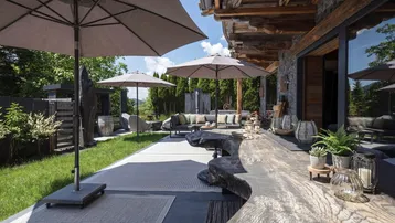 Großzügige Terrasse mit bequemen Lounge-Möbeln, Sonnenschirmen und einem einzigartigen Holztisch im Grünen.