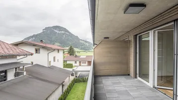 Geräumiger Balkon mit Fliesenboden und schöner Aussicht auf die umliegende Berglandschaft und Häuser.