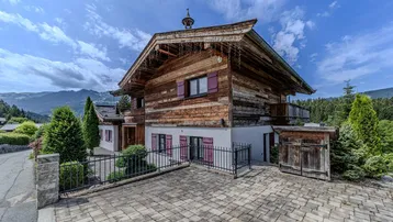 Traditionelles Holzchalet mit Satteldach, roten Fensterläden und gepflasterter Auffahrt in alpiner Umgebung.