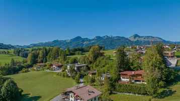 Luftaufnahme eines malerischen Dorfes in den Bergen mit grünen Wiesen und traditionellen Häusern.