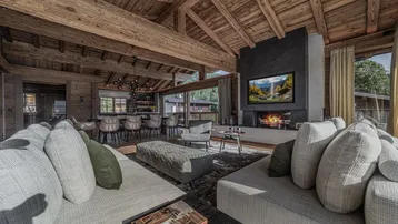 Gemütliches Wohnzimmer mit großem Sofa, modernem Kamin und Holzbalkendecke im Chalet-Stil.