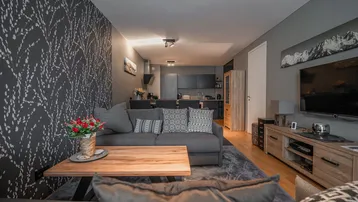 Moderner offener Wohnbereich mit stilvoller Tapete, bequemer Couch und integrierter Küche im Hintergrund.