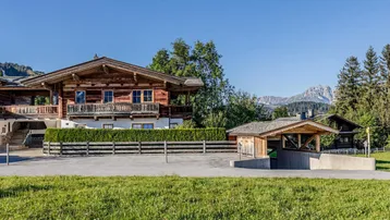 Traditionelles Holzhaus im alpinen Stil mit Balkonen, umgeben von grüner Landschaft und Bergblick.