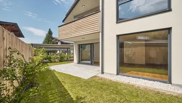 Moderne Gebäudefassade mit Terrasse, Rasenfläche und Zugang zu den Innenräumen.