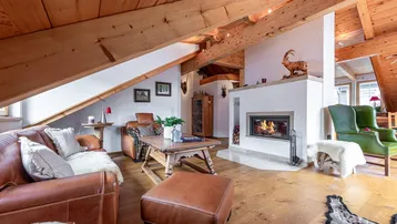 Gemütliches Wohnzimmer im Dachgeschoss mit Holzbalken, Kamin und rustikalen Ledermöbeln.